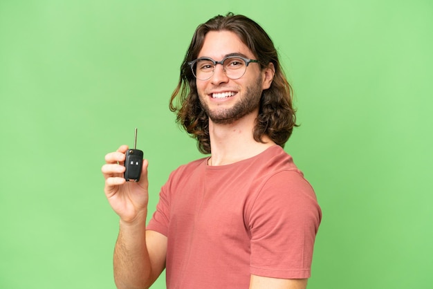 Young handsome man holding car keys over isolated background smiling a lot