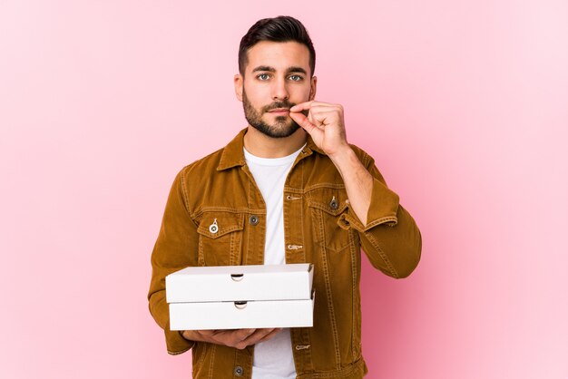 Young handsome man holding pizzas with fingers on lips keeping a secret.