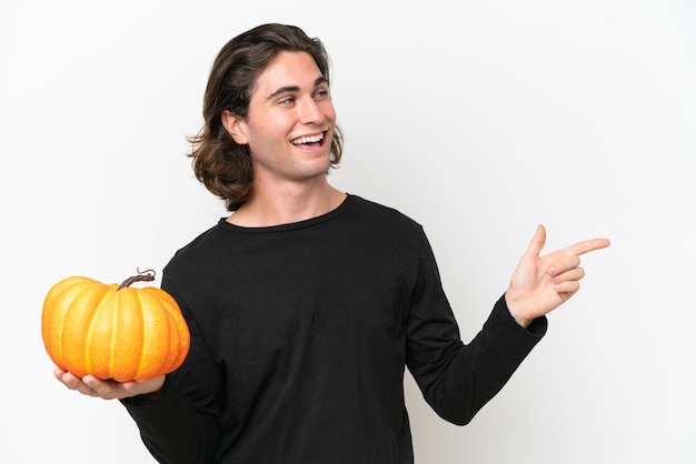 Young handsome man holding a pumpkin isolated on white background pointing finger to the side and presenting a product