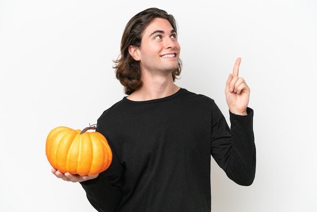 Young handsome man holding a pumpkin isolated on white background pointing up a great idea