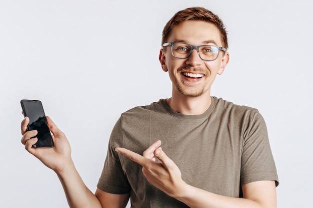 Young handsome man holding a smartphone and smiling on gray isolated space