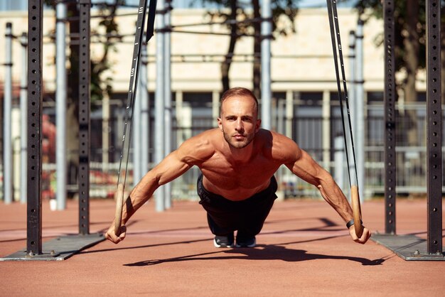 Young and handsome man is doing some pushups he is using loops for that