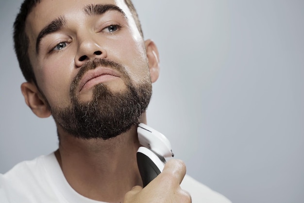 Young handsome man is using electric trimmer for beard shaving