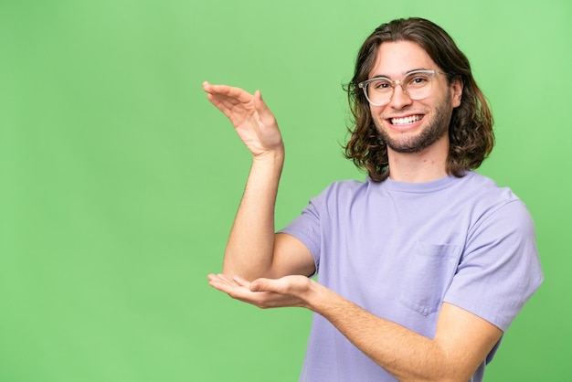 Young handsome man over isolated background holding copyspace to insert an ad