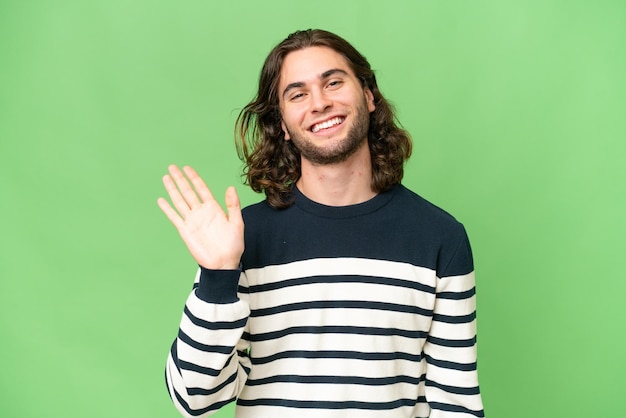 Young handsome man over isolated background saluting with hand with happy expression