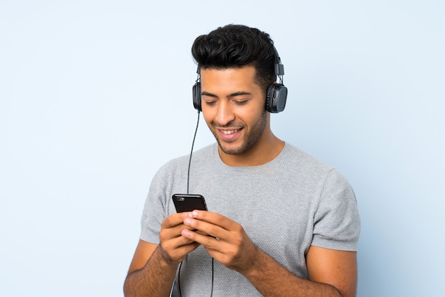 Young handsome man over isolated background using the mobile with headphones