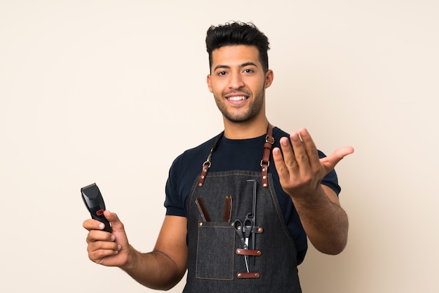 Young handsome man over isolated background with hairdresser or barber dress and holding hair cutting machine