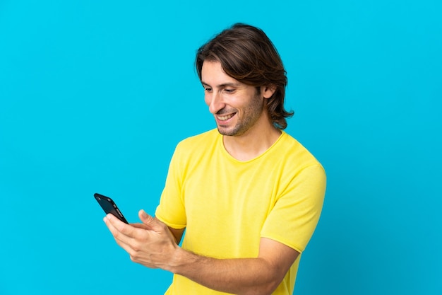 Young handsome man isolated on blue background sending a message or email with the mobile