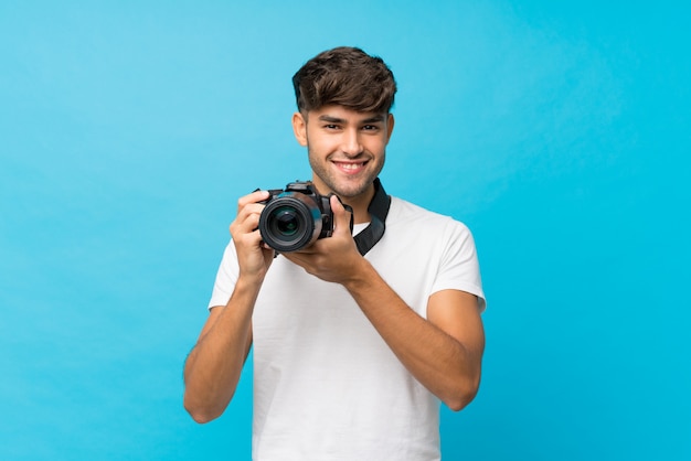 Young handsome man over isolated blue with a professional camera