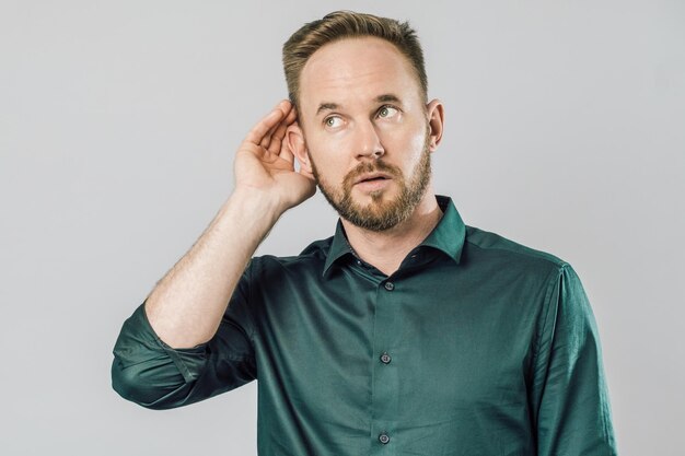 Photo young handsome man over isolated gray background with hand over ear listening and hearing to rumor or gossip