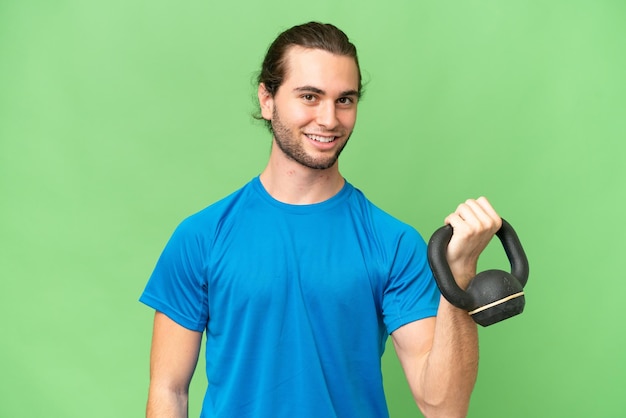 Young handsome man isolated on green chroma background making weightlifting with kettlebell