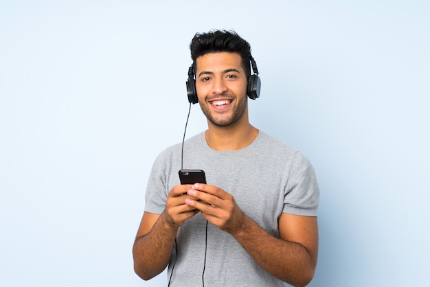 Young handsome man over isolated wall using the mobile with headphones