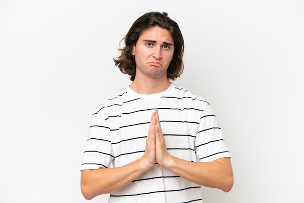 Young handsome man isolated on white background keeps palm together Person asks for something