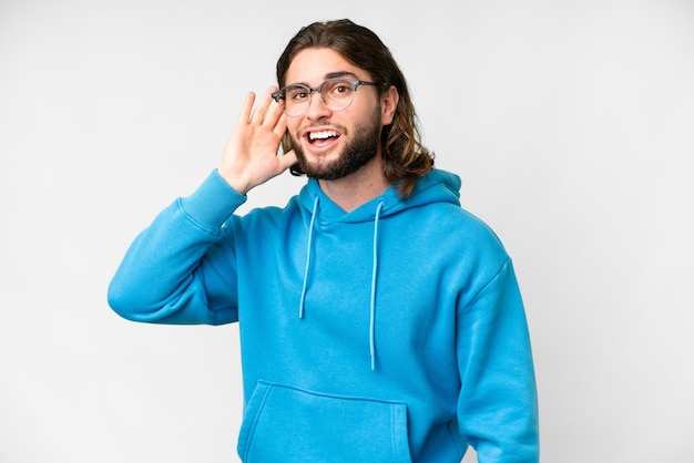 Young handsome man over isolated white background listening to something by putting hand on the ear