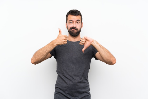 Young handsome man over isolated white wall making good-bad sign. Undecided between yes or not