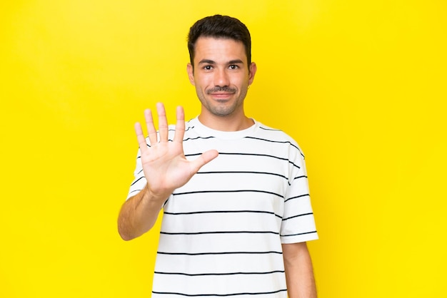 Young handsome man over isolated yellow background counting five with fingers