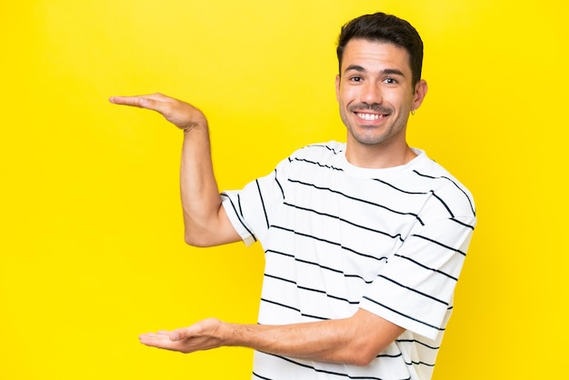 Young handsome man over isolated yellow background holding copyspace to insert an ad