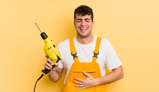 Young handsome man laughing out loud at some hilarious joke handyman and drill concept