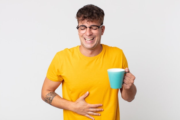 Young handsome man laughing out loud at some hilarious joke and holding a coffe cup