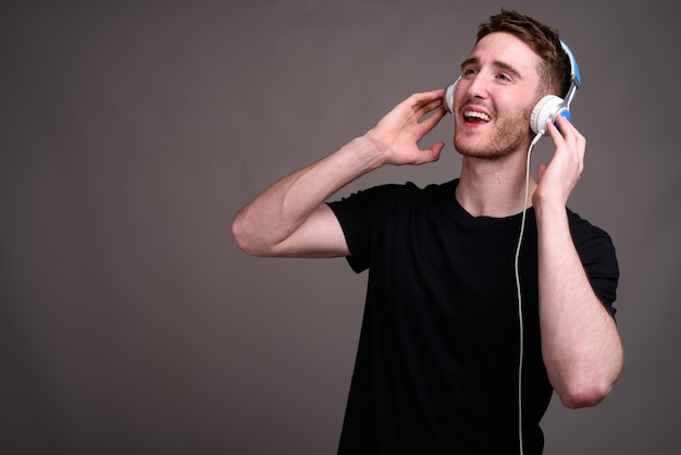 Young handsome man listening to music against gray