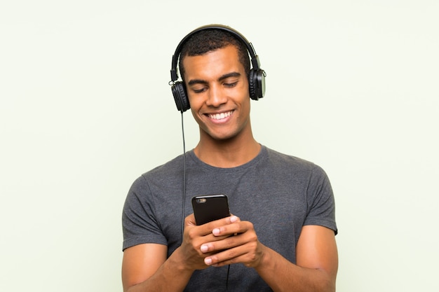 Young handsome man listening music with a mobile over isolated green wall