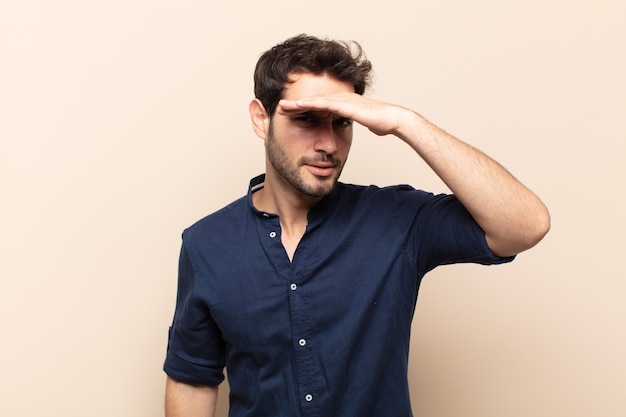 Young handsome man looking bewildered and astonished, with hand over forehead looking far away, watching or searching