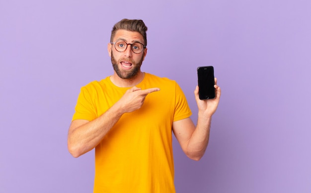 Young handsome man looking excited and surprised pointing to the side. cell concept