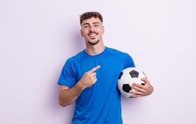 Young handsome man looking excited and surprised pointing to the side. soccer concept