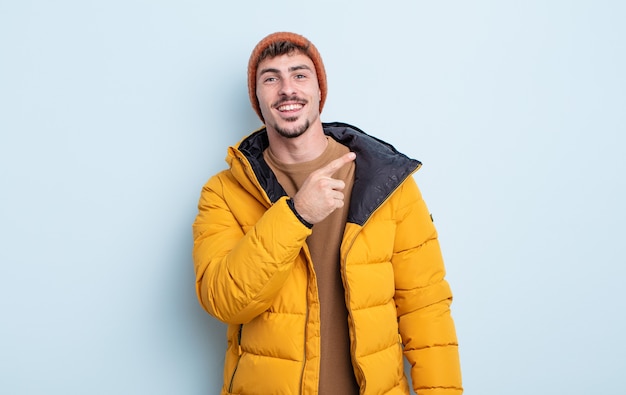 Photo young handsome man looking excited and surprised pointing to the side. winter concept