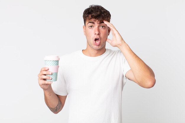 Young handsome man looking happy astonished and surprised and holding a take away coffee