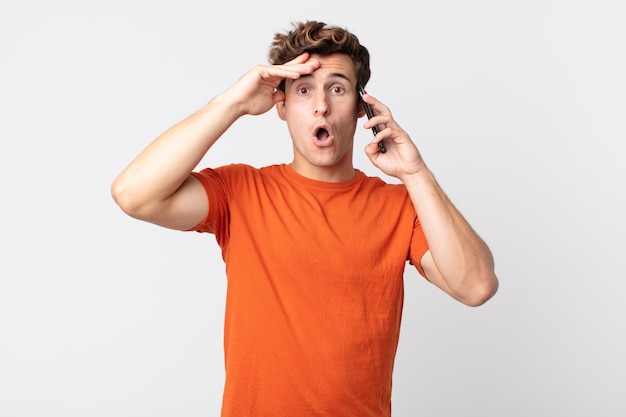 Young handsome man looking happy, astonished and surprised and talking with a smart phone