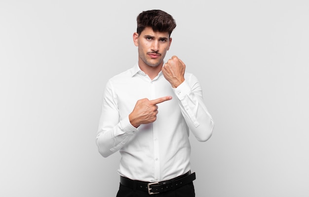 Young handsome man looking impatient and angry, pointing at watch