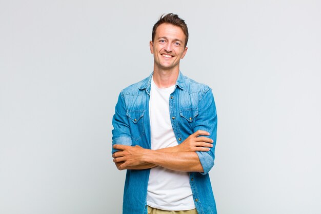 Young handsome man looking like a happy, proud and satisfied achiever smiling with arms crossed