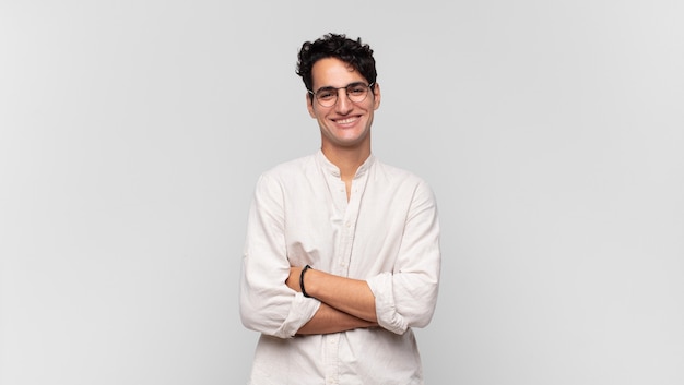 Young handsome man looking like a happy, proud and satisfied achiever smiling with arms crossed