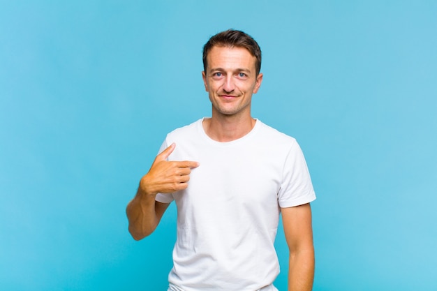 Young handsome man looking proud, confident and happy, smiling and pointing to self or making number one sign