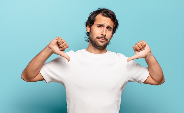 Young handsome man looking sad, disappointed or angry, showing thumbs down in disagreement, feeling frustrated