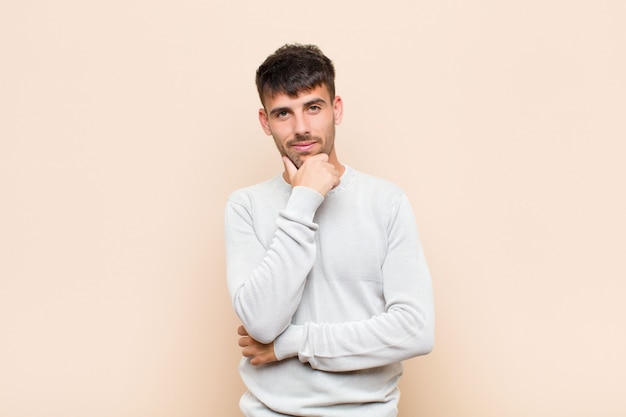 Young handsome man looking serious, confused, uncertain and thoughtful, doubting among options or choices against warm wall