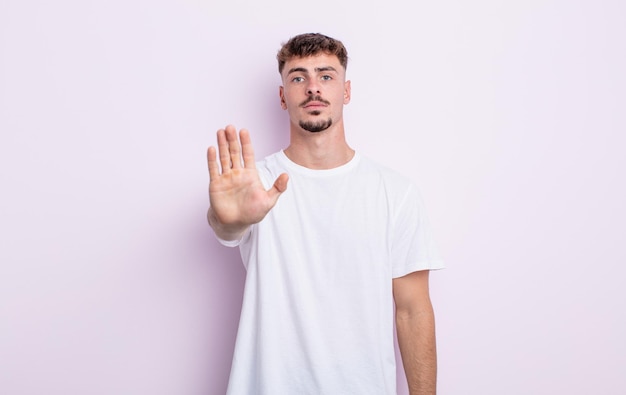 Young handsome man looking serious, stern, displeased and angry showing open palm making stop gesture