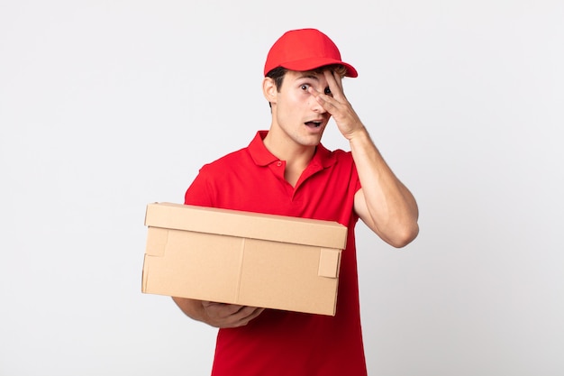 Young handsome man looking shocked, scared or terrified, covering face with hand delivery package service concept.