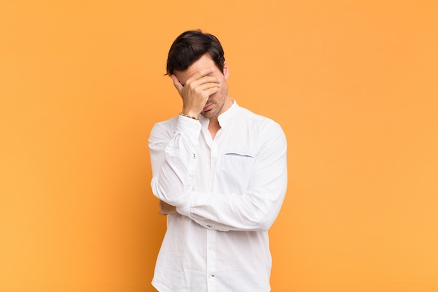 Young handsome man looking stressed, ashamed or upset, with a headache, covering face with hand