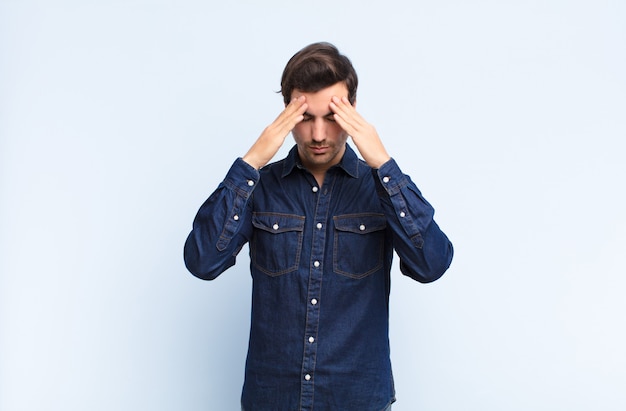 Young handsome man looking stressed and frustrated, working under pressure with a headache and troubled with problems against blue wall