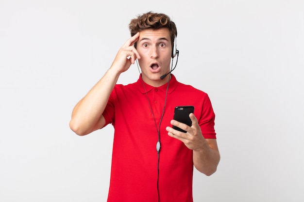 Young handsome man looking surprised, realizing a new thought, idea or concept with a smartphone and headset