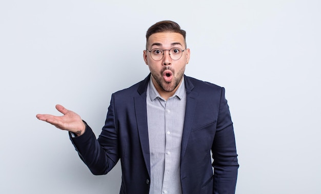 Young handsome man looking surprised and shocked, with jaw dropped holding an object. businessman concept