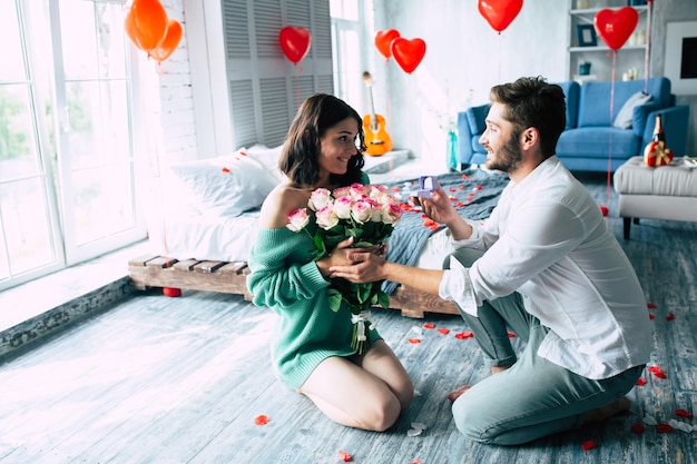 Young handsome man makes a proposal to his beautiful girlfriend to marry him in a beautiful bedroom with a romantic background. Husband and wife