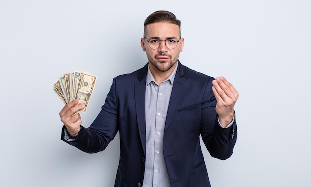 Young handsome man making capice or money gesture, telling you to pay. dollar banknotes concept