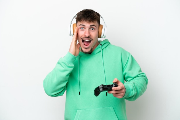 Young handsome man playing with a video game controller isolated on white background with surprise and shocked facial expression