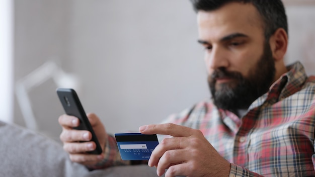 Young handsome man shopping online holding credit card, sitting at home. Online banking app service.