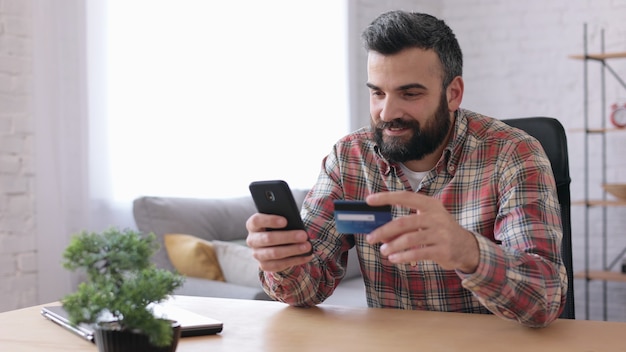 Young handsome man shopping online holding credit card, sitting at home. Online banking app service.