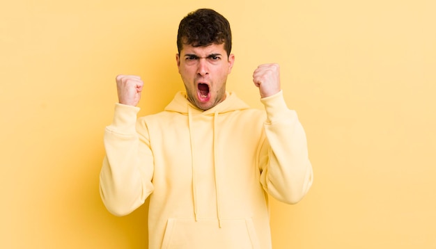 Young handsome man shouting aggressively with an angry expression or with fists clenched celebrating success