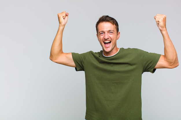 Young handsome man shouting triumphantly, looking like excited, happy and surprised winner, celebrating